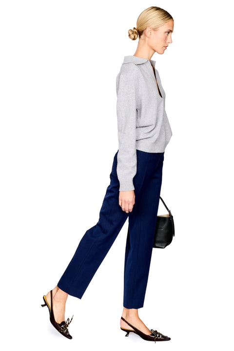A woman modeling a light gray long-sleeve knit top and navy blue wide-leg cropped trousers, styled with black pointed-toe slingback flats and a small black handbag, against a plain white background.