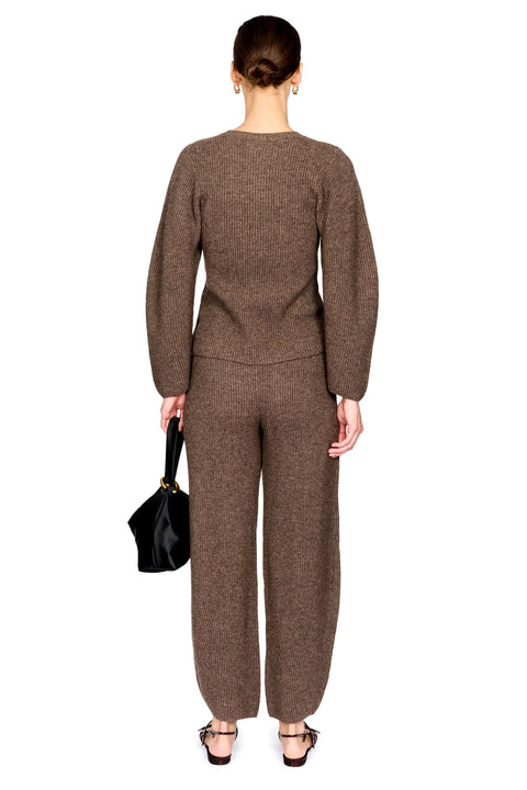 A model shown from the back wearing a matching brown knit long-sleeve top and wide-leg trousers set, holding a black handbag against a plain white background.