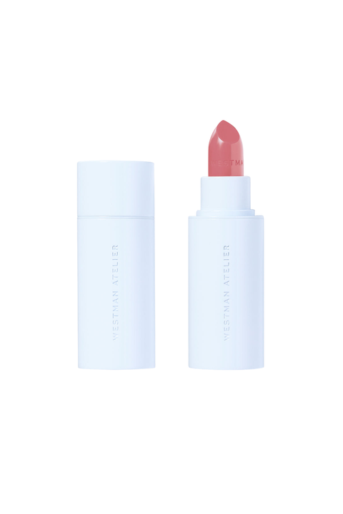 A lipstick by Westman Atelier in a pale pink shade, shown with its white cap off and standing next to the closed white cap on a solid white background.