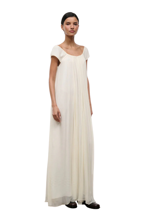 A woman wearing a long ivory dress with short cap sleeves and an elastic neckline side angle