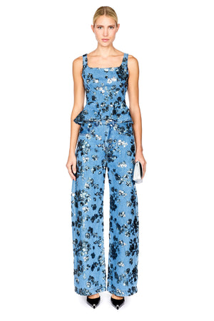 A model wearing a sleeveless denim floral top with a peplum waist with matching jeans, photographed against a solid white background.
