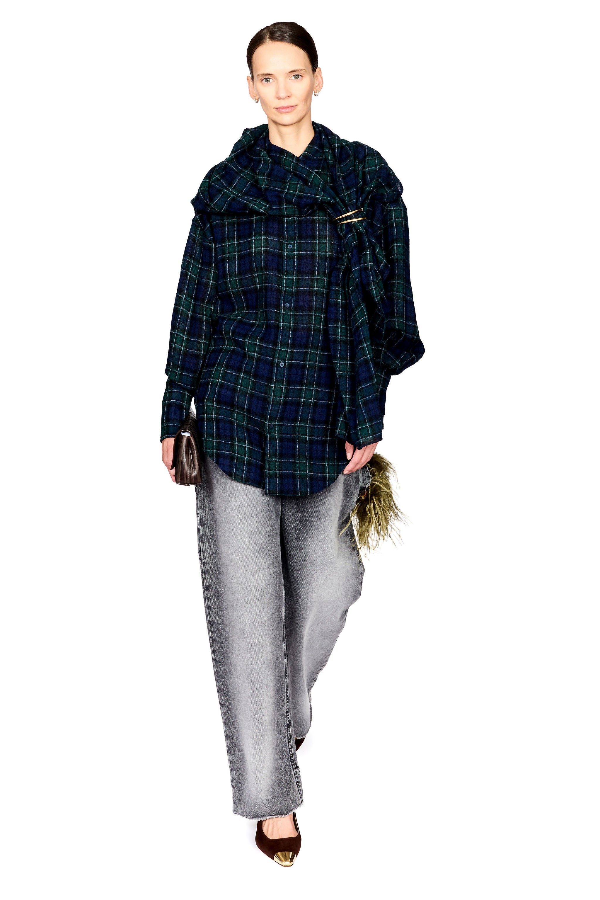 A model wearing a dark green and black plaid oversized shirt jacket with wide lapels, paired with light gray wide-leg jeans and brown pointed shoes, standing against a plain white background.