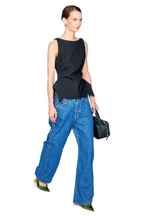 A model wearing a sleeveless black peplum top, wide-leg blue jeans, olive green pointed shoes, and holding a small black handbag against a plain white background.