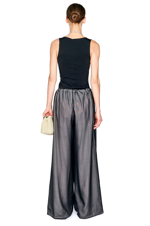A model shown from the back wearing a sleeveless black top and wide-leg charcoal gray pinstriped trousers, holding a small beige clutch against a plain white background.
