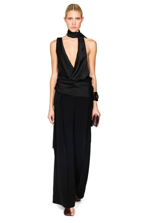 A model wearing a black satin halter-neck wrap top and matching wide-leg trousers, styled with a black choker, a black cuff bracelet, and a small black clutch, set against a plain white background.