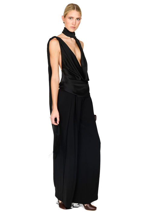 A model wearing a black sleeveless top and matching pants with a high neck, draped wrap-style bodice, and wide-leg pants, photographed against a plain white background.