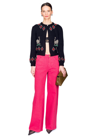 Woman wearing a black embroidered cardigan and pink pants on a white background
