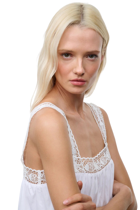 Woman wearing a white flowy mini dress with a lace fish-embroidered trim on a white background close up