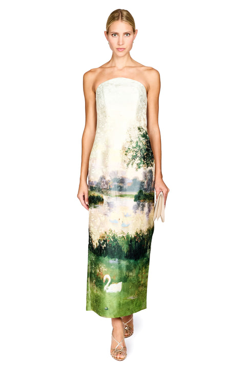 A strapless maxi dress with a landscape print featuring a lake, trees, a white swan, and birds, modeled on a white background.