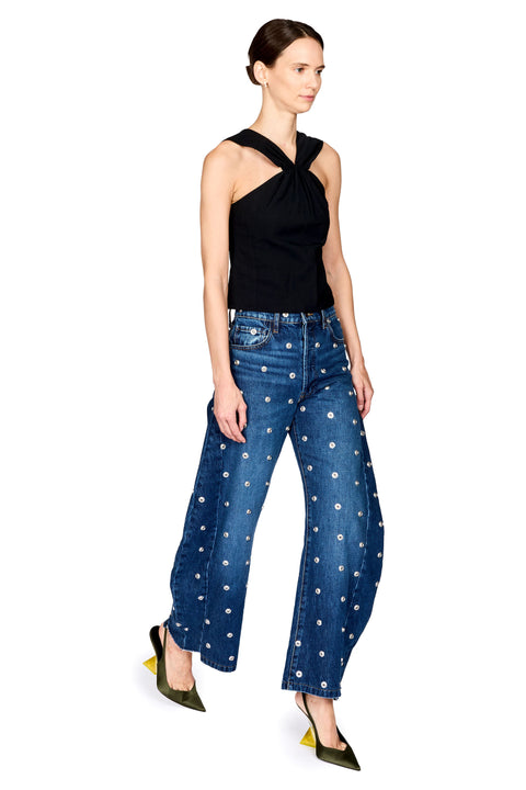 A model wearing a black halter top and blue wide-leg jeans with a white floral pattern, paired with olive green pointed-toe heels, against a plain white background.