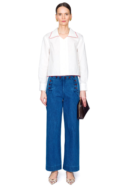 Woman wearing a white blouse with red accents and blue jeans with red buttons on a white background
