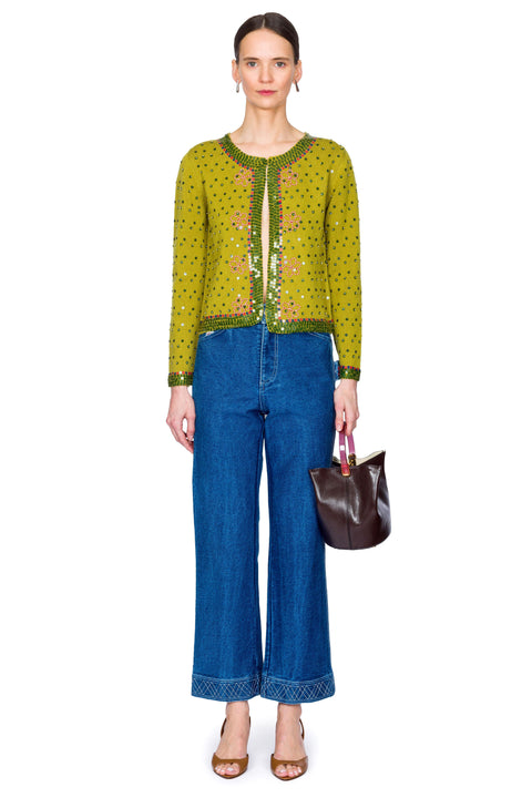 Woman wearing a green patterned top and blue jeans, holding a brown handbag on a white background from a centered view.