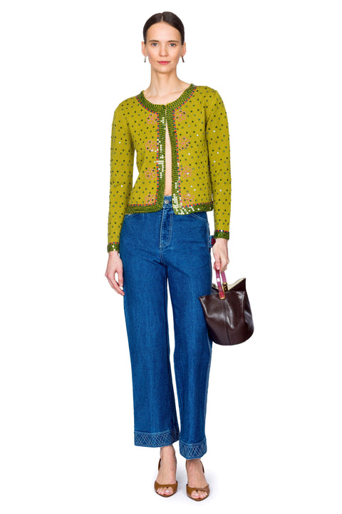 Woman wearing a green patterned top and blue jeans, holding a brown handbag on a white background.