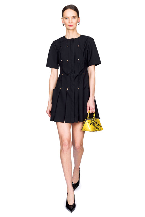Woman wearing a short black origami dress with a yellow snakeskin bag with one foot in front of the other.