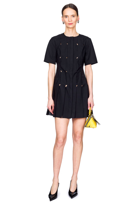 Woman wearing a short black origami dress with a yellow snakeskin bag in a centered stance.