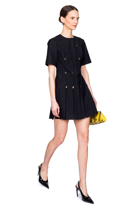 Woman wearing a short black origami dress with a yellow snakeskin bag from the side view.