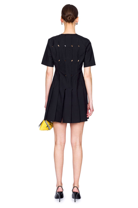 Woman wearing a short black origami dress with a yellow snakeskin bag from the back.