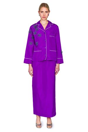 Woman wearing a purple button down pajama shirt with floral embellishments and a matching maxi skirt.