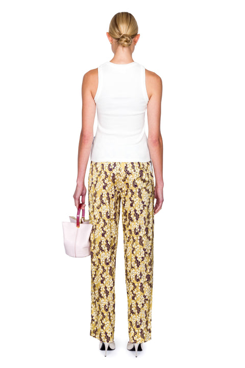 Back-facing woman wearing a white embellished top with circular cutouts and pajama style yellow pants with ornate shapes.