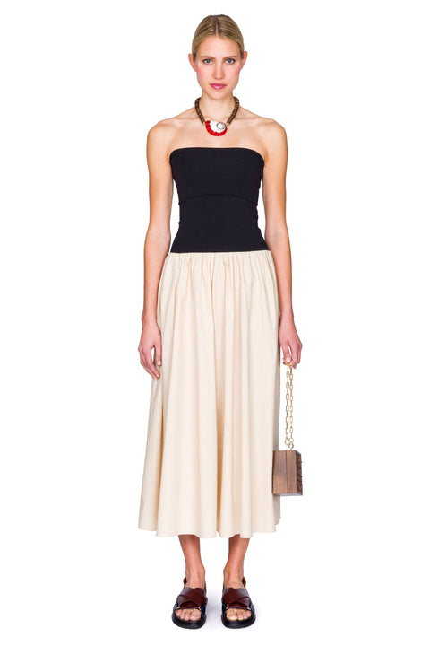 Woman wearing a black and beige dress with a handbag on a white background.