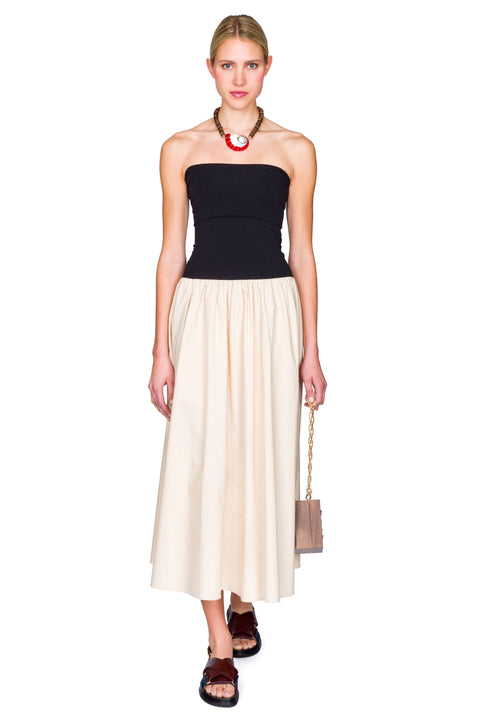 Woman wearing a black and beige dress with a handbag on a white background with one foot in front of the other.