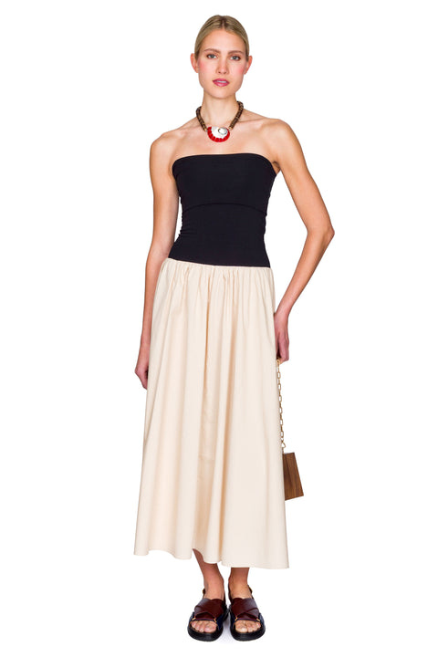 Woman wearing a black and beige dress with a handbag on a white background with hand on her hip.
