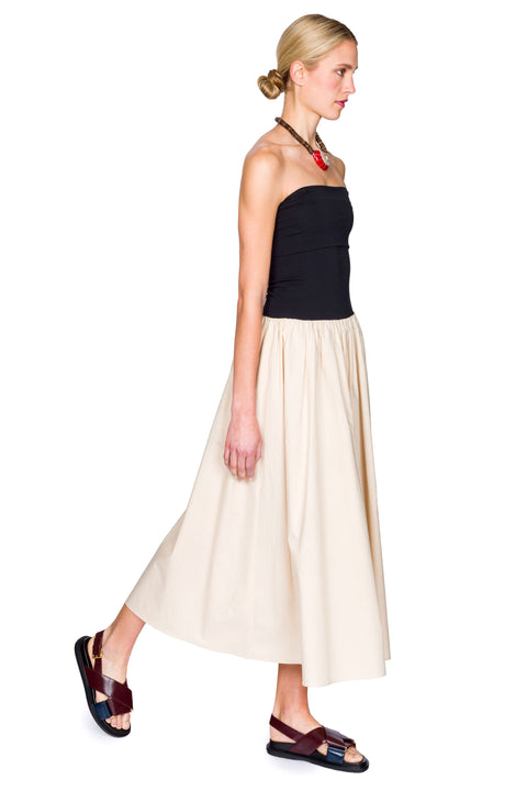 Woman wearing a black and beige dress with a handbag on a white background from the side view.