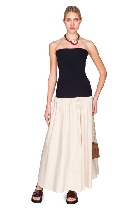Woman wearing a black and beige dress with a handbag on a white background with hand on her hip.