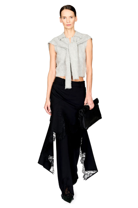 A model wearing a light gray sleeveless cropped wrap top, black high-waisted trousers with black lace inserts, and holding a black clutch bag against a solid white background.
