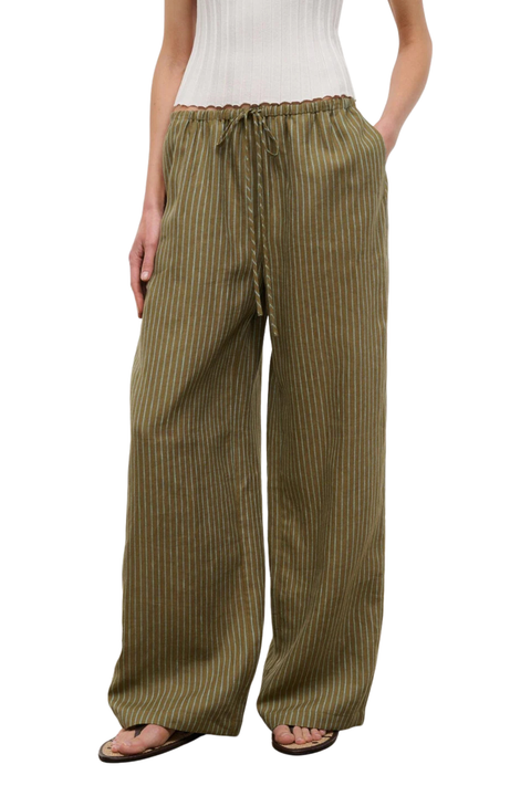 Woman wearing a white top and green striped linen beach pants on a white background