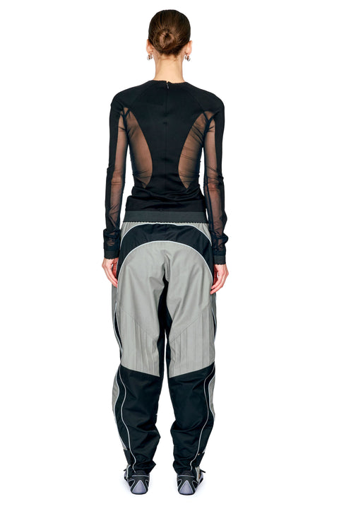 A model shown from the back wearing a black long-sleeve top with sheer mesh side panels and light gray and black wide-leg pants, against a plain white background.
