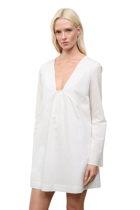 Close-up of a woman wearing a low cut, long sleeve white mini dress